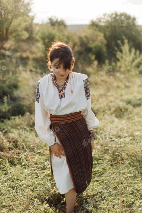 Preview: Young woman in traditional national embroidered shirt and skirt on nature at sunset.