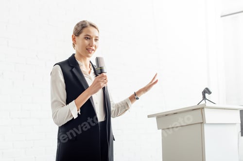 Preview: attractive businesswoman holding microphone and talking during conference in conference hall