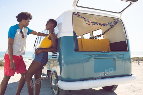 Preview: Happy African american couple talking with each other near camper van at beach in the sunshine