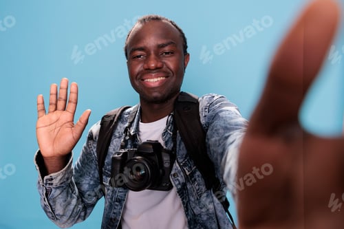Preview: Smiling young man waving at camera while taking selfie photo