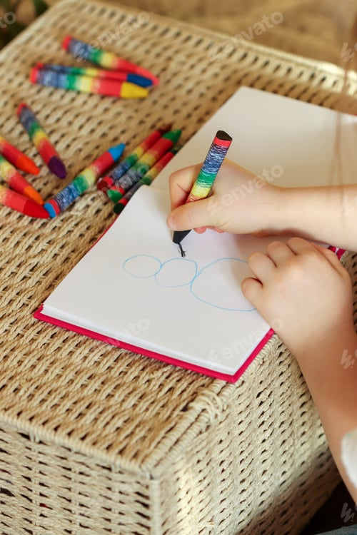 Preview: Little girl 6 years old draws with wax crayons in a sketch book