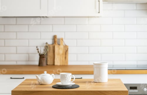 Preview: Wooden oak table with a cup of tea in front of the kitchen with a white brick background.