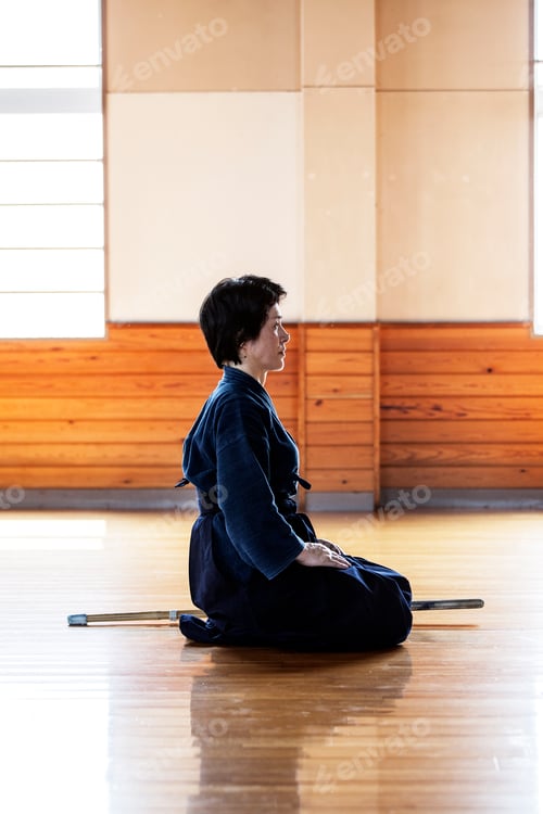 Preview: Side view of female Japanese Kendo fighter kneeling on wooden floor.