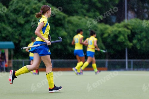 Preview: Young sportswoman playing field hockey under the rain