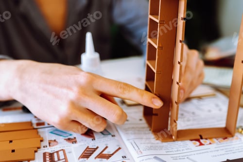 Preview: female hands assembling wooden architectural model using glue in bright room