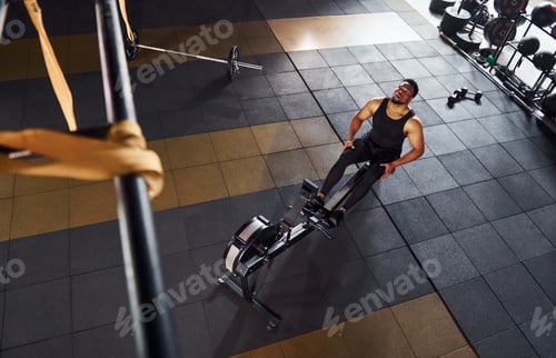 Preview: Strong african american man in sportive clothes have workout day in the gym and using equipment