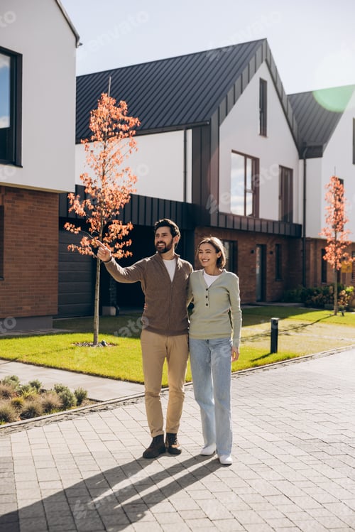 Aperçu: Smiling happy couple investing in new modern house, man pointing finger looking away