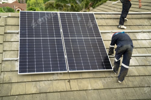 Preview: Men technicians mounting photovoltaic solar moduls on rooftop of warehouse.