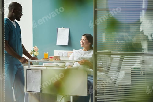 Preview: Pregnant Caucasian Woman Smiling While Talking with Black Male Nurse in Hospital