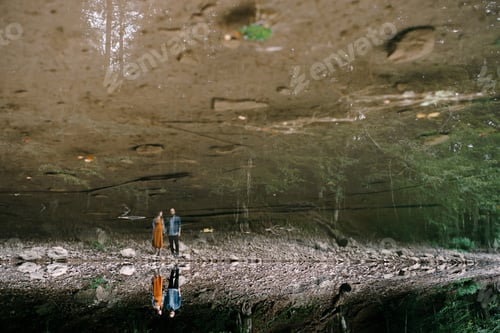 Preview: Woman with a man stands on a rocky slope by the lake, reflecting in clear water