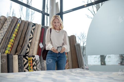 Preview: Smiling woman photographing carpet on the smartphone in the store.