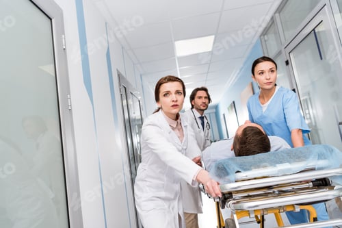 Preview: Worried doctors and nurse transporting unconscious patient on gurney