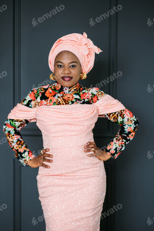 Preview: Portrait of charming African woman wearing stylish pink dress and turban on head, smiling on camera