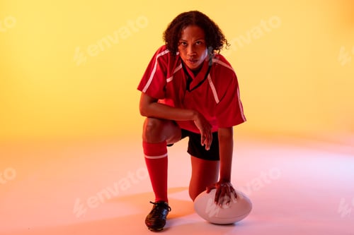 Preview: Portrait of african american female rugby player with rugby ball over neon yellow lighting