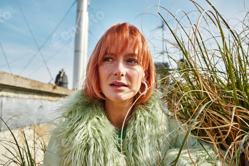 Preview: modern woman in trendy casual clothes looking away near decorative plants on roof terrace in Vienna