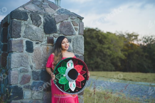 Preview: Mexican woman wearing traditional hat and dress. Outdoor portrait next to stone wall.