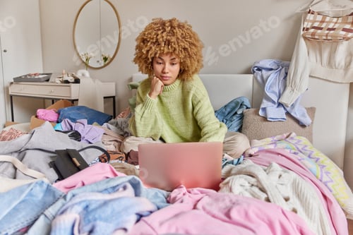 Preview: Photo of serious curly haired woman reorganizes her wardrobe sells second hand clothes on resail