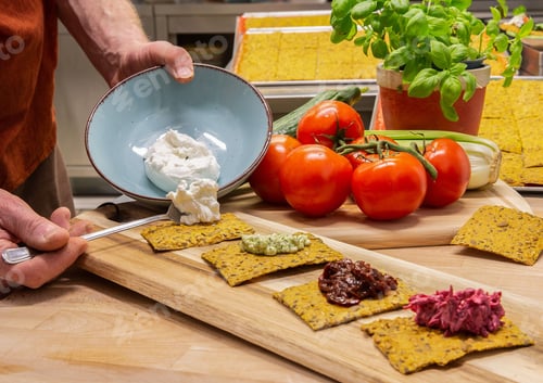 Preview: Person adding a topping on crispbread in the kitchen.