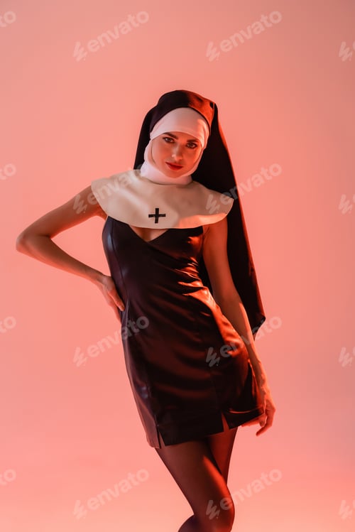 Preview: sexy nun in black leather dress posing with hand on hip isolated on pink
