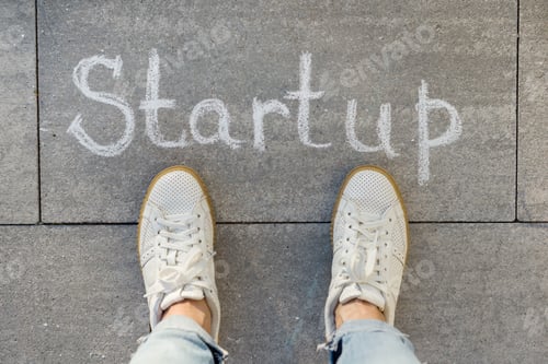 Preview: View from above, female feet with text startup written on grey sidewalk