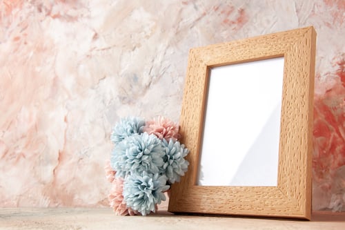 Preview: Top view of brown empty wooden photo frame standing on table and flower on the left side on nude