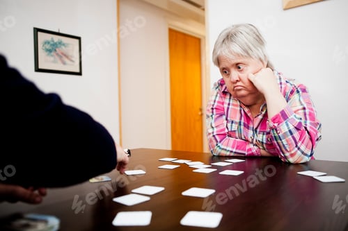 Preview: Woman with down syndrome looking at friend arranging cards on table