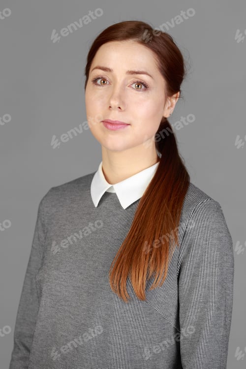 Preview: Young woman with long brown hair wearing a gray top poses against a gray background