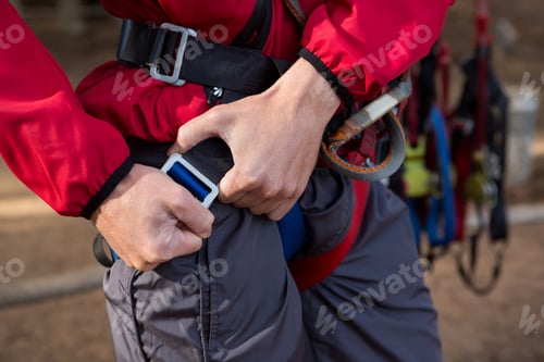 Preview: Young hiker man adjusting his harness in the forest on a sunny day