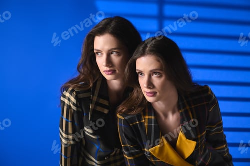 Preview: Stylish twin sisters showcase their unique fashion sense against a vibrant blue backdrop