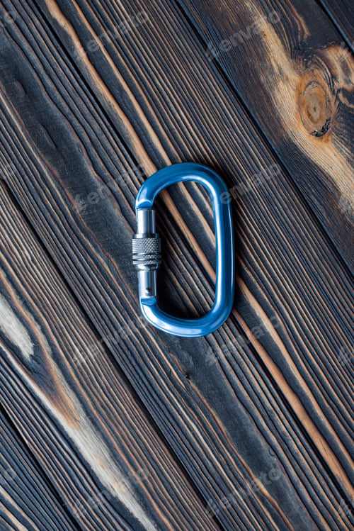 Preview: Steel material. Isolated photo of climbing equipment. Part of carabiner lying on the wooden table