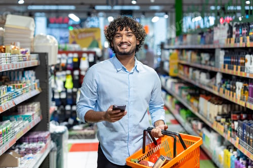 Preview: A happy man smiles while holding a shopping basket in a busy grocery store aisle.
