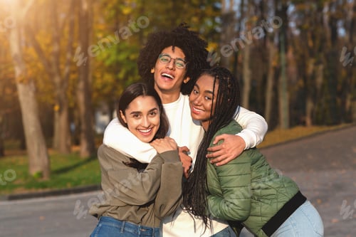 Preview: Cheerful african guy hugging his smiling girlfriends