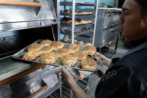 Preview: A young Hispanic baker is pulling a tray full of fresh baked sweet breads from the oven