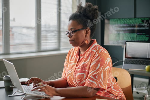 Preview: Young Adult Black Woman Developing Software on Laptop in Contemporary Office