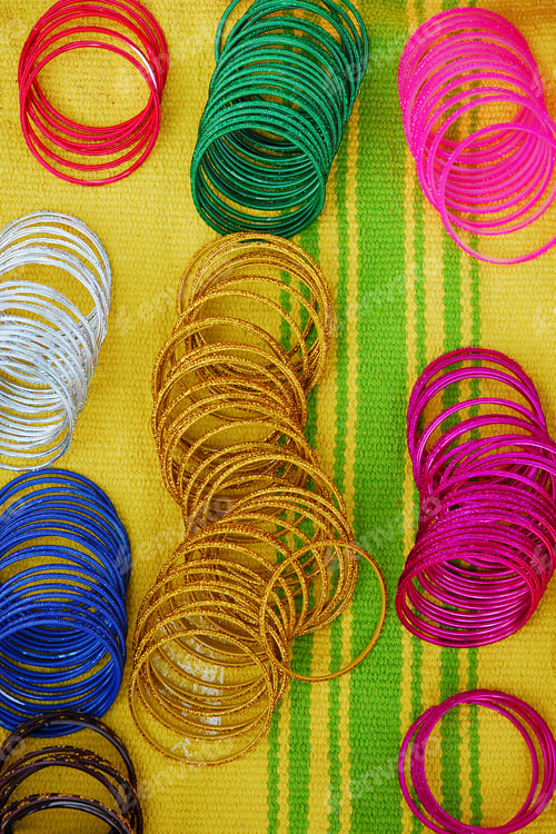 Preview: Coloured bangles paid out on a yellow and green striped background.