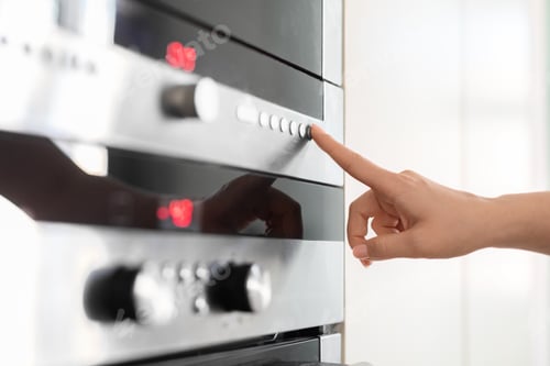 Preview: Female hand touching control panel on electric oven in kitchen