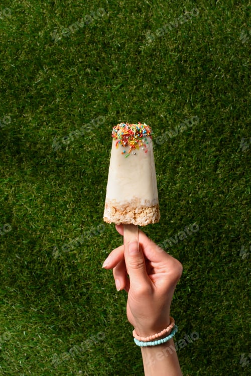 Preview: Female hand with sweet Popsicle on green grass background