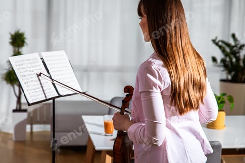 Preview: Young woman practicing playing the violin at home.
