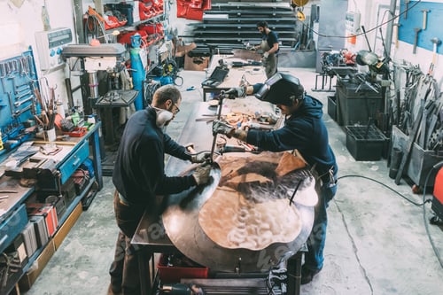 Preview: Male metalwork team hammering copper at forge workbench
