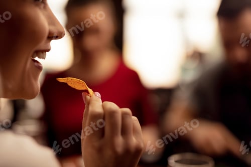 Preview: Close up of happy woman eating nacho chips in a pub.
