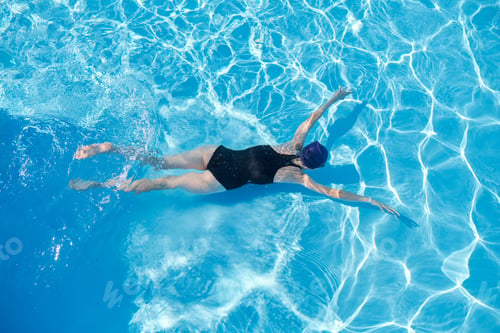 Preview: Young woman swimming underwater in an outdoor pool, top view of back of girl
