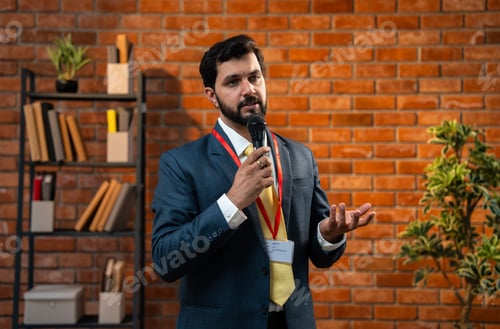 Preview: Bearded Indian CEO giving formal speech using mic while standing in cozy office environment