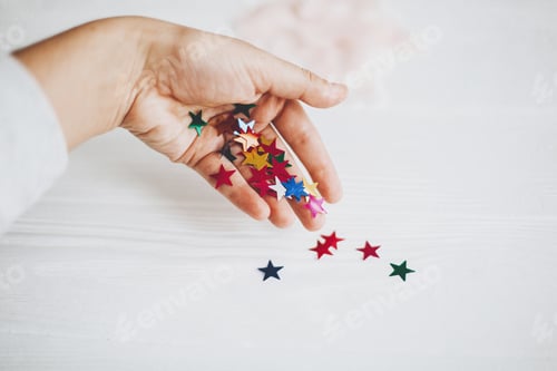 Preview: Hand holding colorful sparkling stars decorations on white background