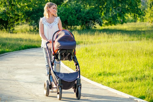 Preview: beautiful and young woman mother and baby in a stroller walking in the park