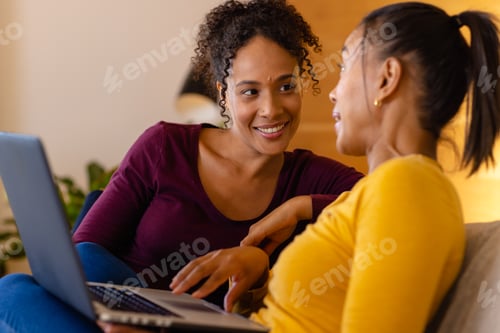Preview: Happy biracial lesbian couple using laptop on sofa in living room