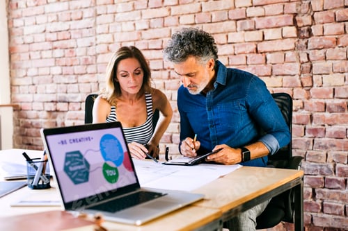 Preview: Colleagues with laptop, plan and notebook working at desk in office