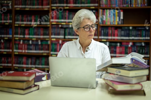 Preview: Elder woman sitting enjoys reading book in quiet of the library