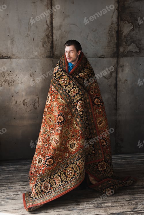 Preview: handsome young man covered in rug in front of concrete wall