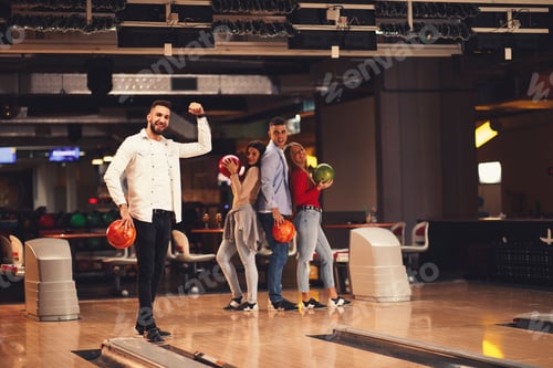 Preview: Beautiful group of young people posing in a bowling alley with a ball in their hand