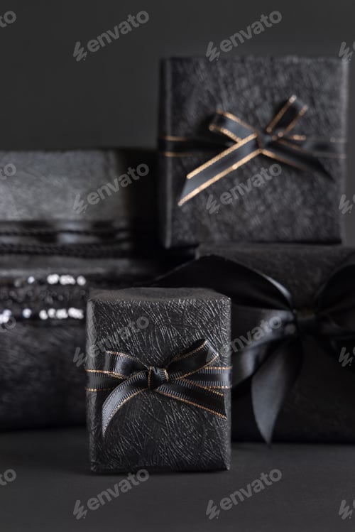 Preview: Wrapped Black Gift Boxes with a ribbon bow on black close up. Black Friday concept